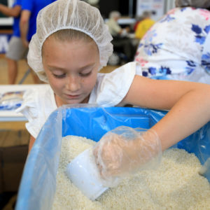 A young girl scoops rice for the MannaPack meals packed by volunteers at a Join The Pack event.