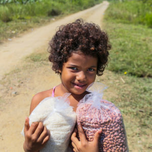 A child in Honduras holds a bag of rice and a bag of beans.
