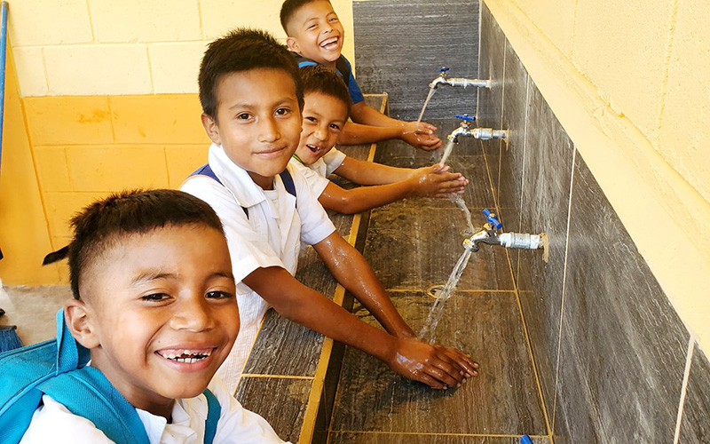 A group of smiling children joyfully washing their hands at a sink.