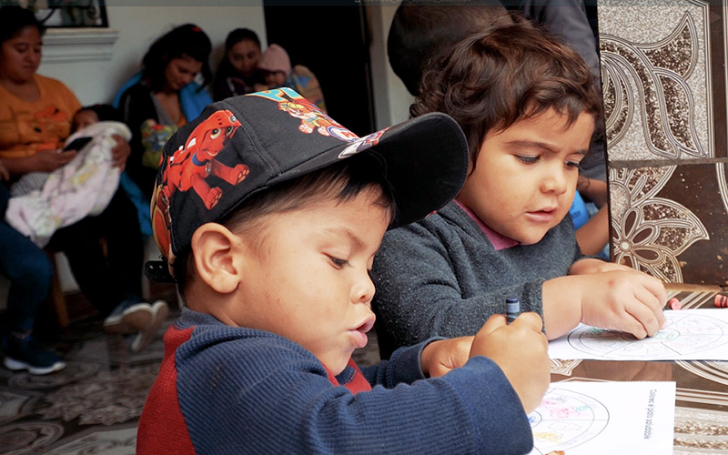 Two children are drawing on paper with crayons.