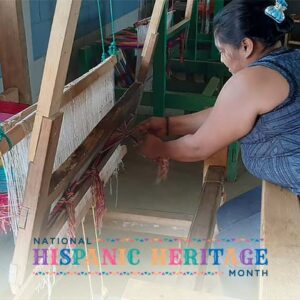 A Honduran woman weaves colorful fabric on a wooden loom.