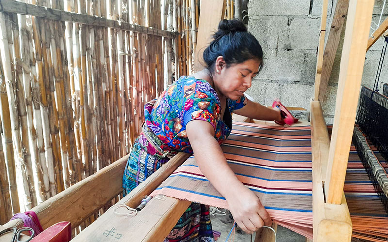 A woman skillfully weaves colorful threads into a piece of cloth on a traditional loom. 