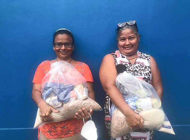  Two women stand side by side, each holding a bag of food, smiling.
