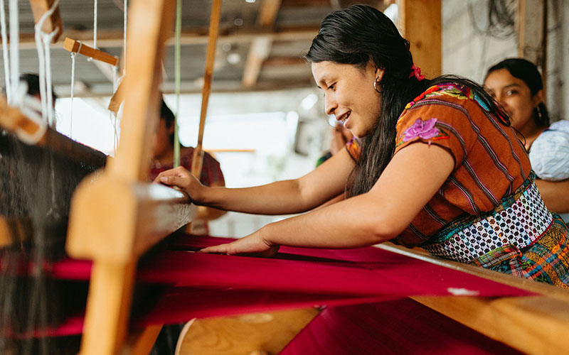 A woman skillfully operates a weaving machine.