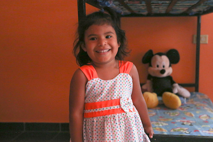 A smiling young girl with a mickey mouse plush in the background