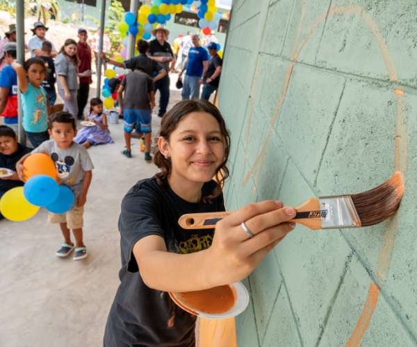 Young girl paints a design on a wall of a sustainable community building