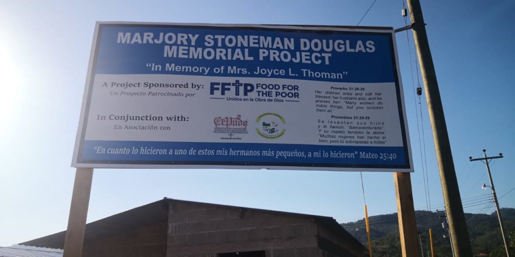 A sign outside the community in Villanueva, Honduras, proclaims: “Marjory Stoneman Douglas Memorial Project. In Memory of Mrs. Joyce L. Thoman.”