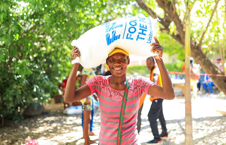 A woman carries a bag of goods from Food For The Poor on her head, smiling, charity, how to deduct donations in 2026