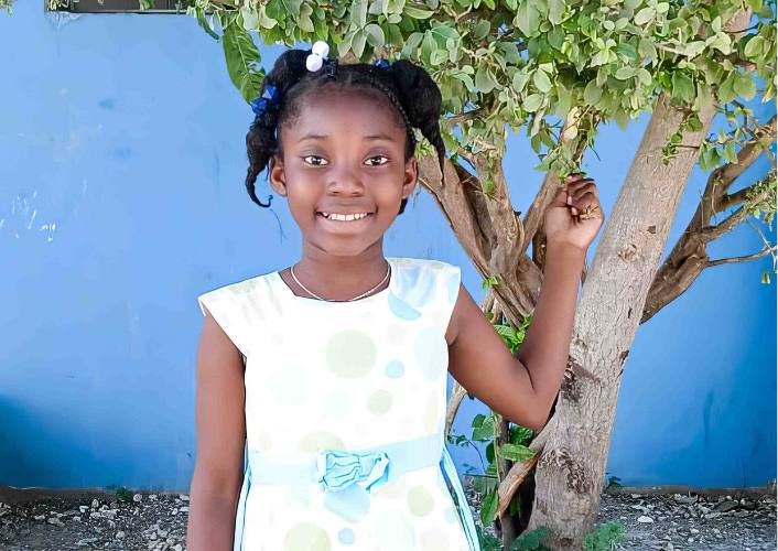 young girl part of the angels of hope place to call home in Haiti poses by a tree