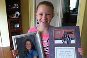 Abby stands with photos of her deceased aunt and the family who have a Food For The Poor home because of Abby.