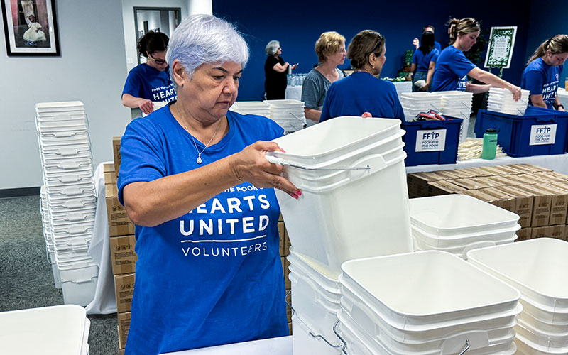 A woman in a blue shirt is placing items into a large white bucket, focused on her task.