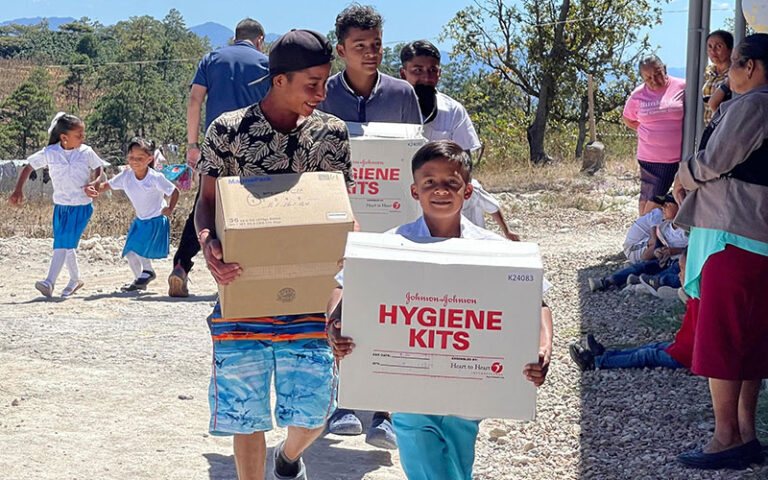 A diverse group of people carrying boxes filled with hygiene kits.