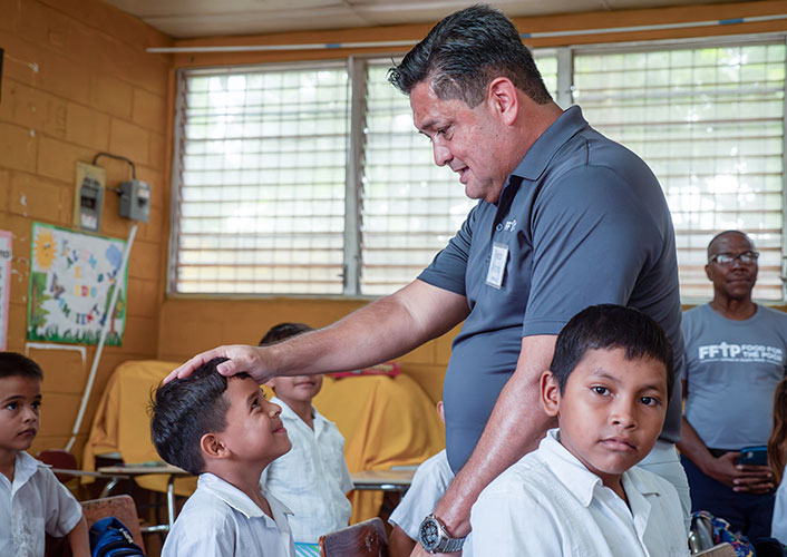 A man assists a child with a learning activity in a classroom setting.