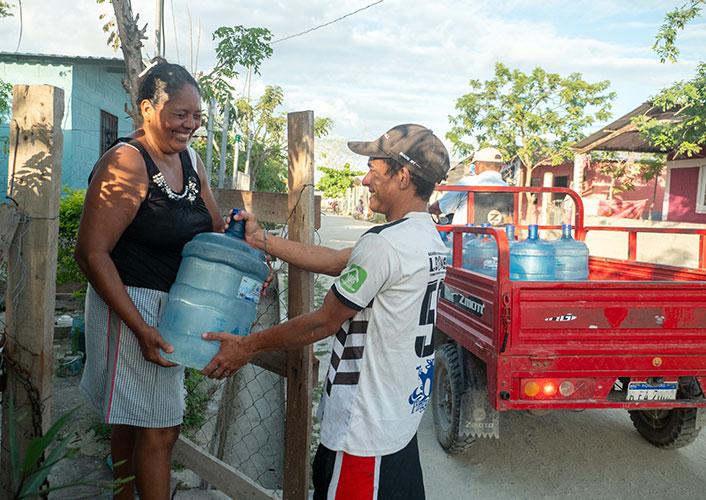 A woman is passing a water container to a man in a collaborative and supportive gesture.