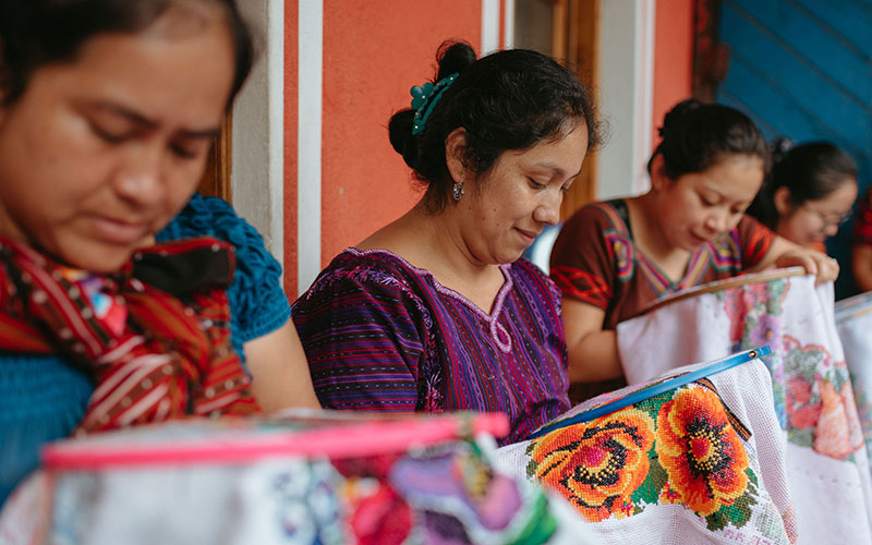 A collective of women focused on sewing a piece of fabric.