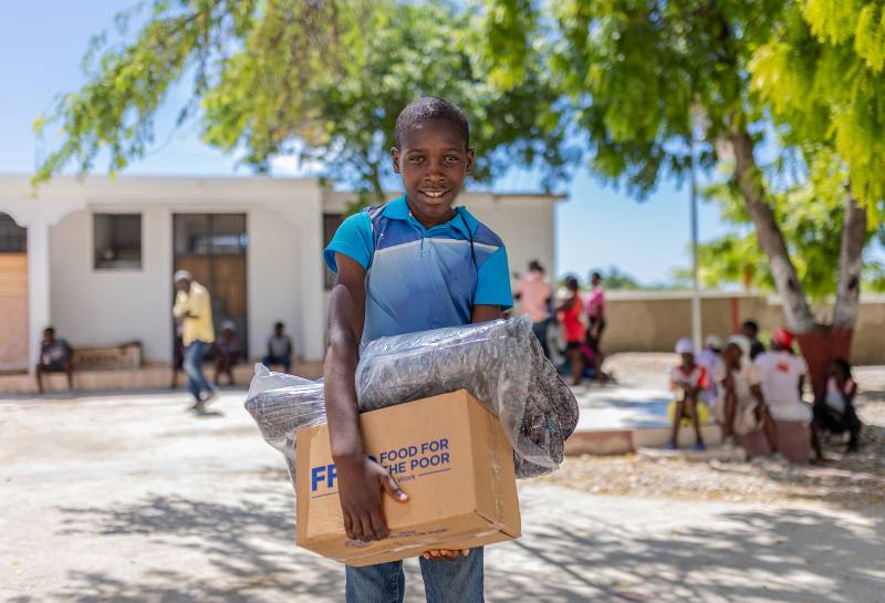 A young boy in Haiti holds a box of disaster relief supplies from Food For The Poor