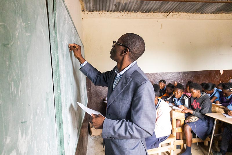 A teacher in Haiti writes on a chalkboard as students write in their notebooks.