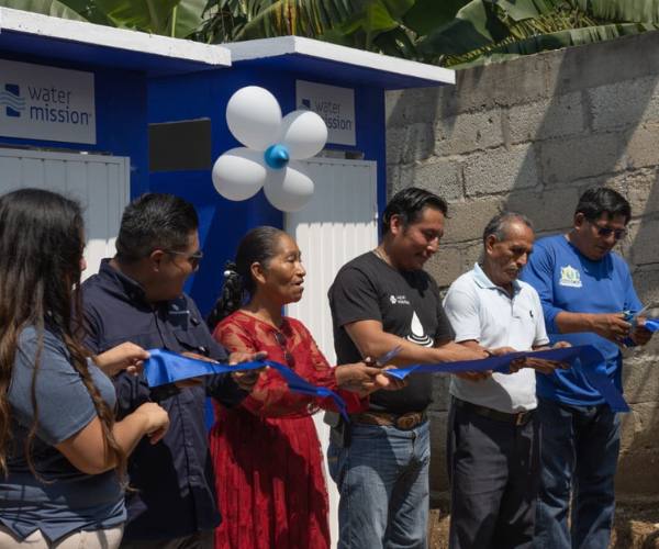 Water Mission team members cut a ribbon in front of new sanitation facilities for FFTP and Water Mission safe water