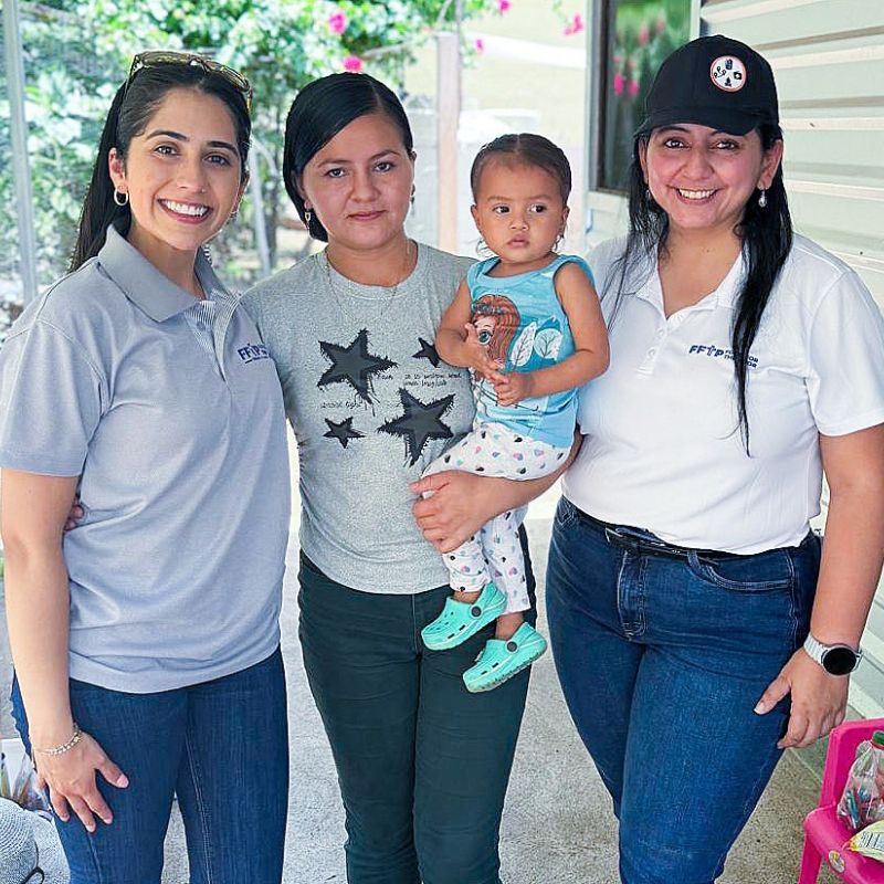 A mother holds her baby daughter while standing in between two women, smiling