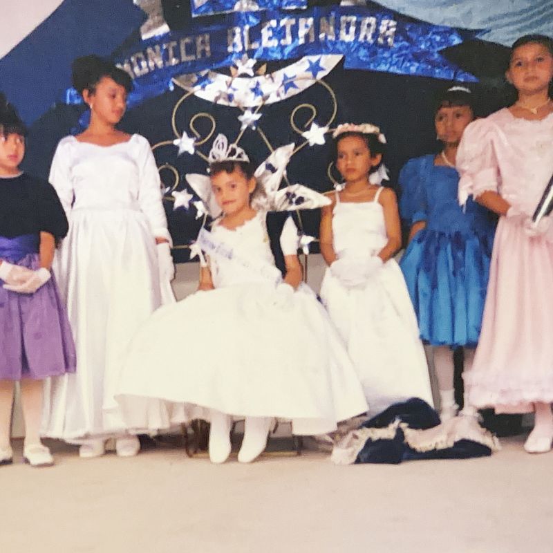 Monica sits in a white dress and crown with classmates