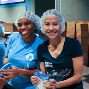 Two women in hairnets hold bags of MannaPack as FFTP Join The Pack volunteers