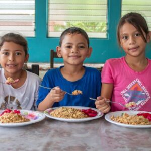 3 smiling children sit at a table with a plate of food in front of them giving tuesday donations