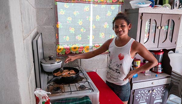 A happy recipient of a new Food For The Poor house built in the sustainable housing community of Los Achiotes, Honduras, cooks in her kitchen.