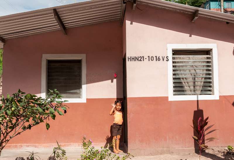 A young girl waves hello from the doorway of her home in Honduras
