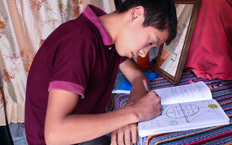 A young man is focused on writing in a notebook, with a pen in hand.