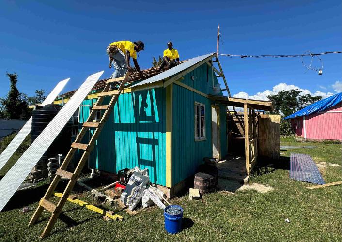 Two men repairing a roof damaged by Hurricane Melissa part of long-term recovery in Jamaica