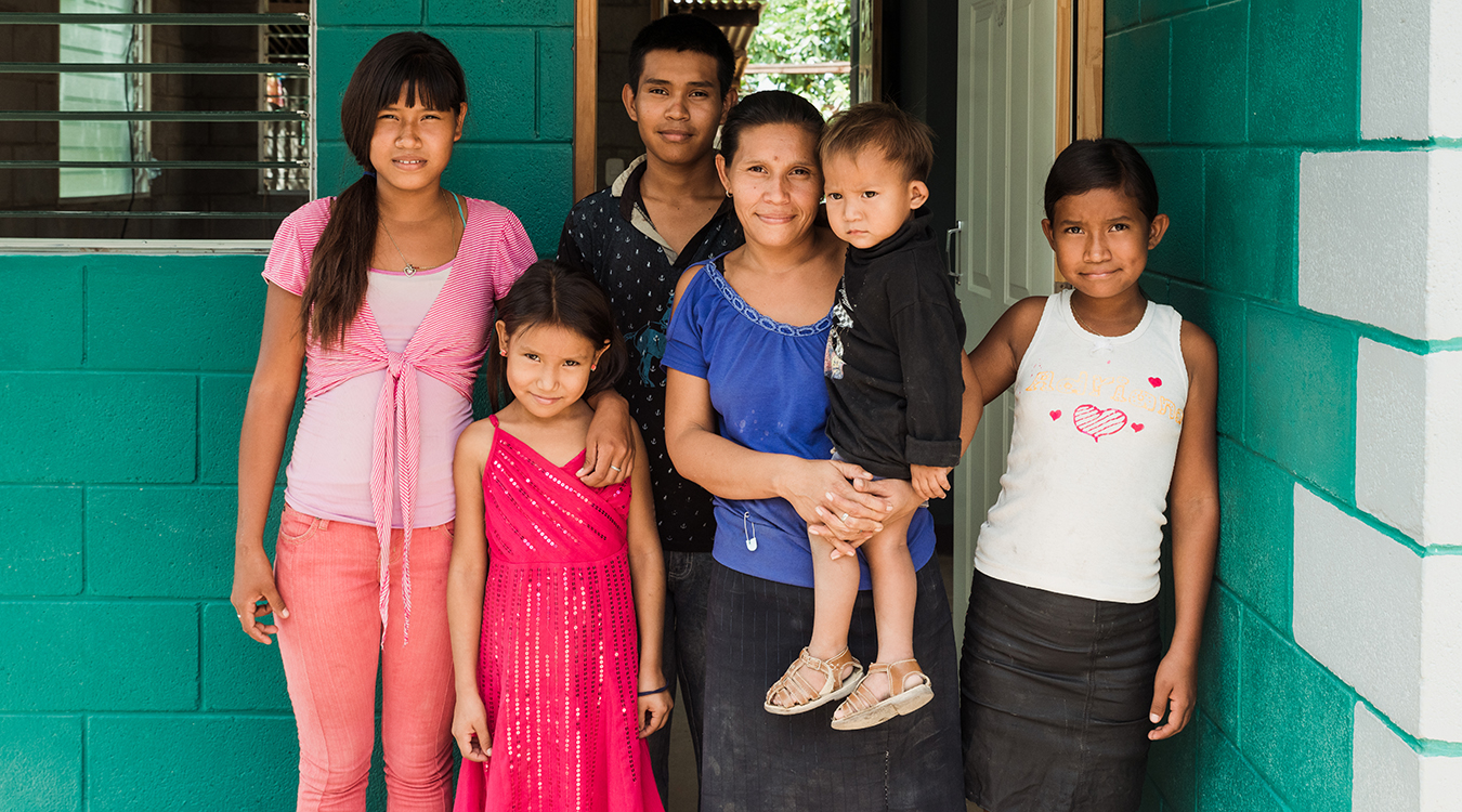 Maria and her children standing outside their new home in Latin America.
