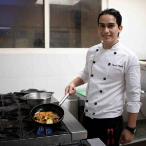 David stands in front of a stove, cooking with his chef uniform