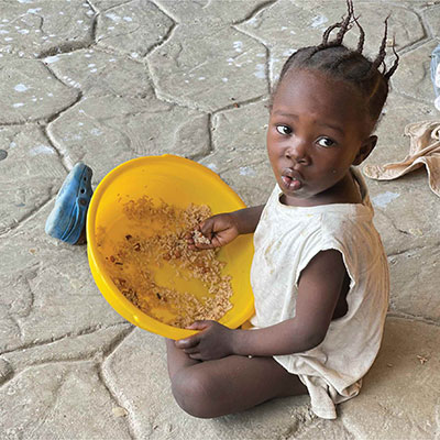 Young Haitian girl sits on the ground with a bowl of food