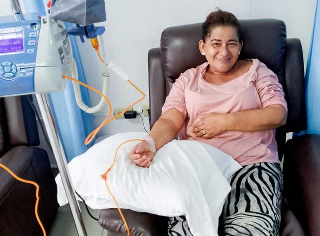 A woman seated in a chair, receiving treatment from an IV machine beside her.