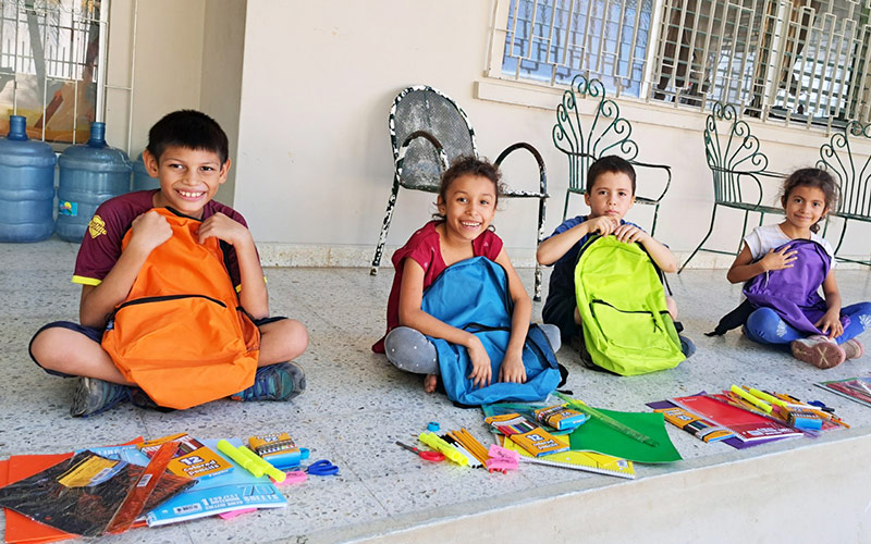 Children sitting on the ground with colorful backpacks received through FFTP Angels of Hope sponsoring a child program