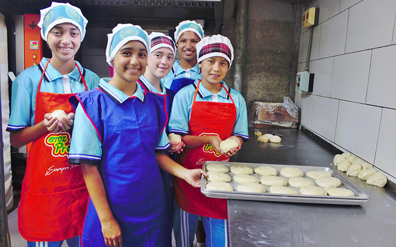 A group of people in aprons gathers around a tray of dough.