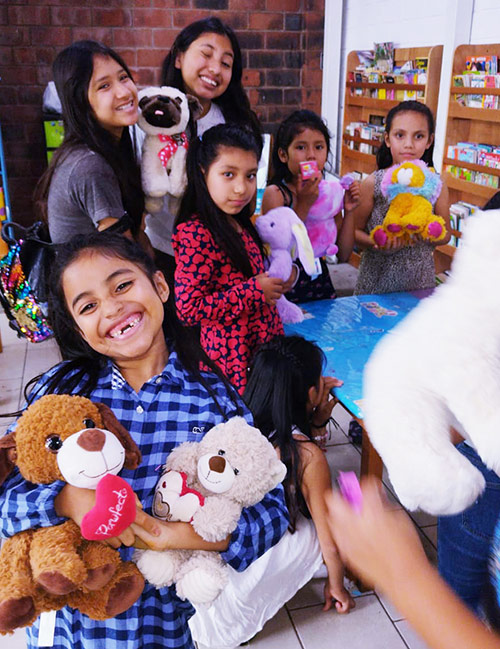 A group of smiling children holding various stuffed animals, sponsoring a child provides gifts