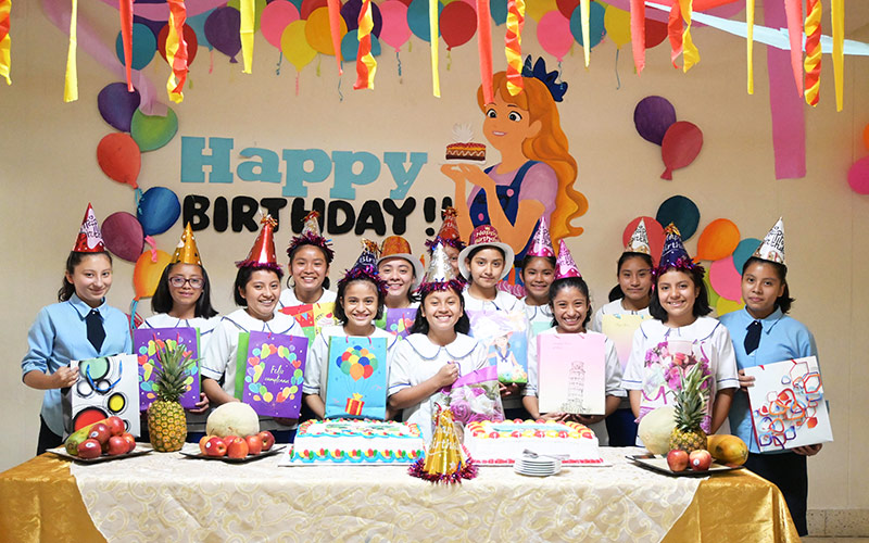 Children gather around a birthday cake, smiling and posing for a cheerful group photo, sponsoring a child helps fund celebrations