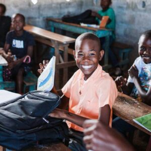 A young boy sits at a desk, smiling, ready to go to learn at a village of hope school food for the poor